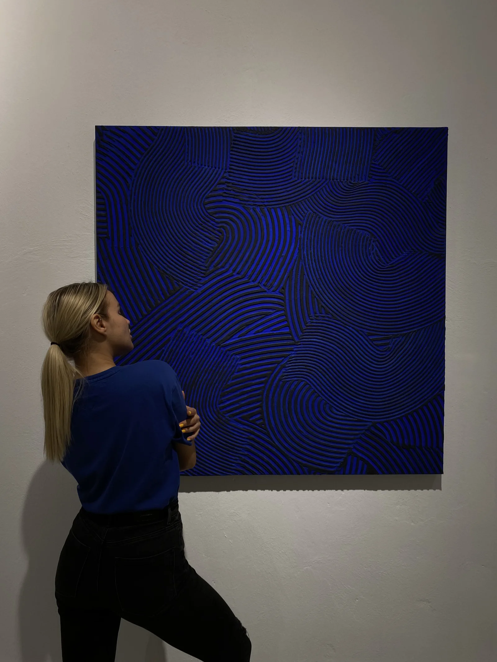 Yana Chi standing before her cobalt combed relief painting in a gallery