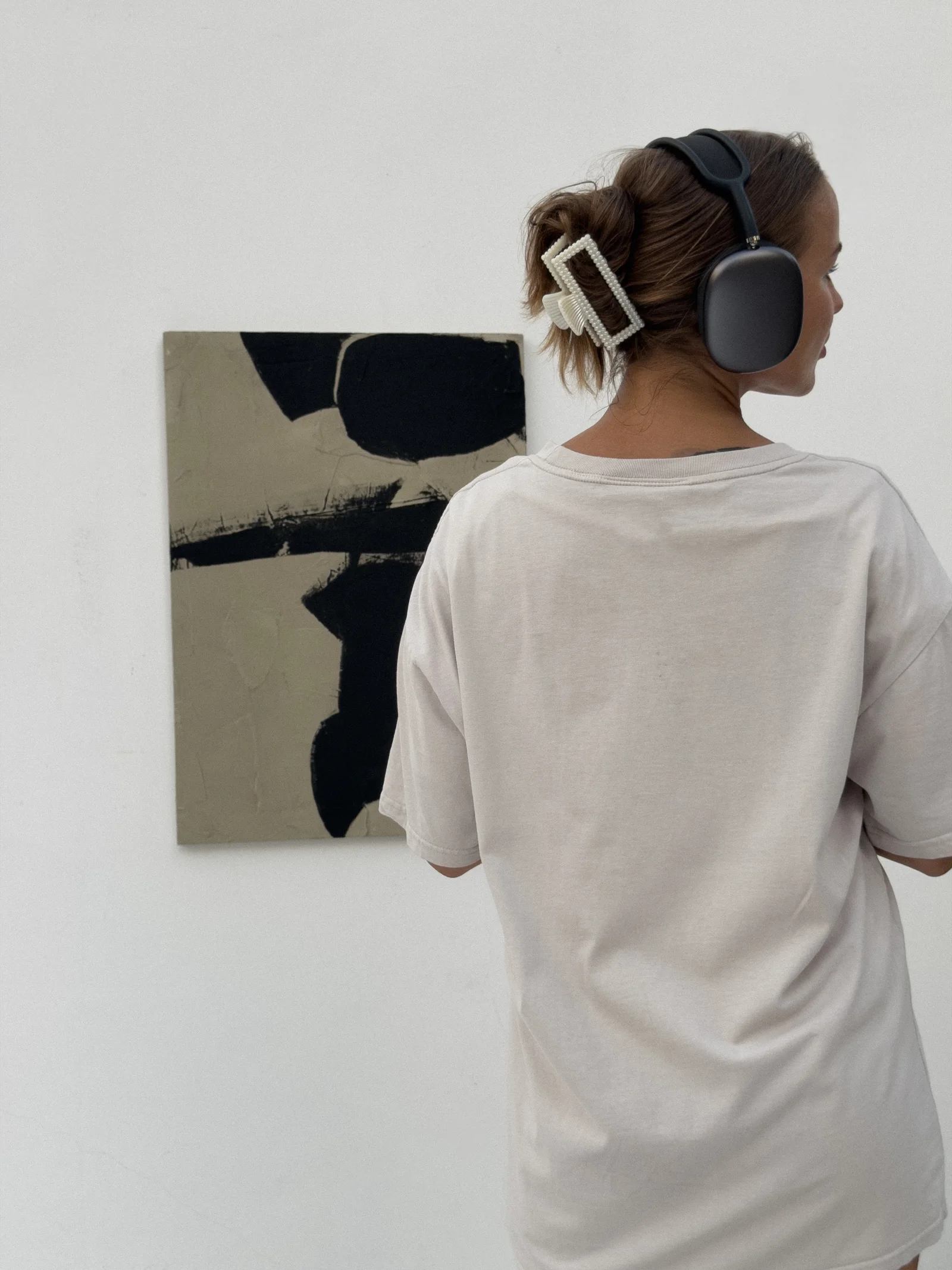 Yana Chi with headphones studying a black and taupe abstract on a white wall