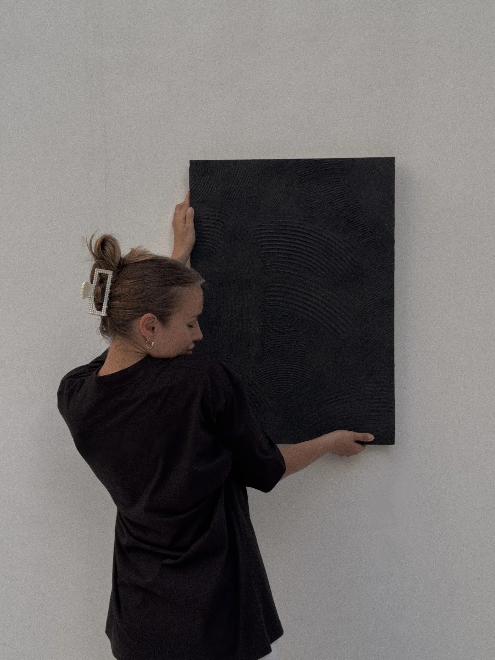 Yana Chi holding a black combed relief panel against the wall, eyes closed